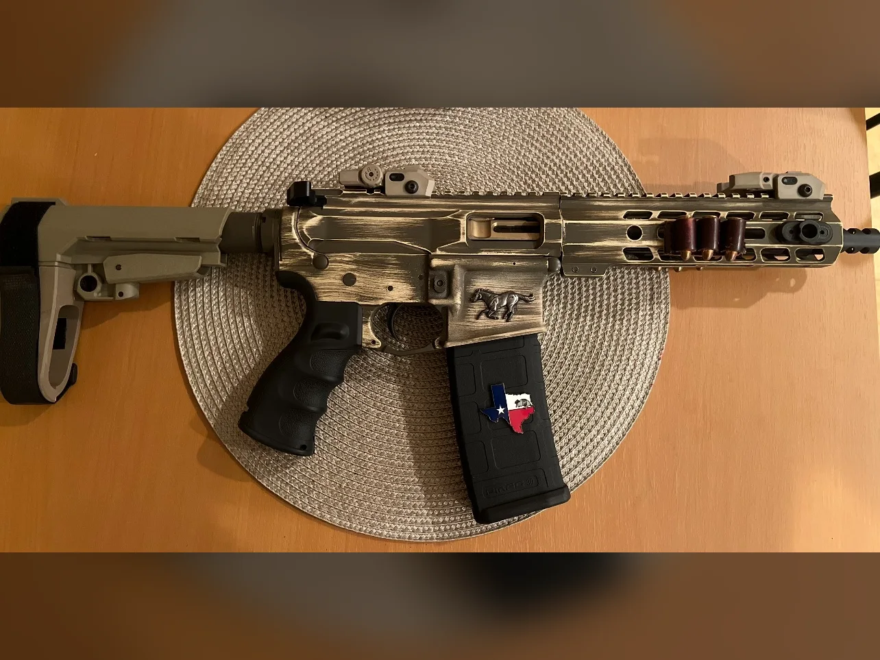 Battleworn tan Cerakote AR-15 pistol with a mustang emblem and Texas magazine badge by Tattoo Tactical