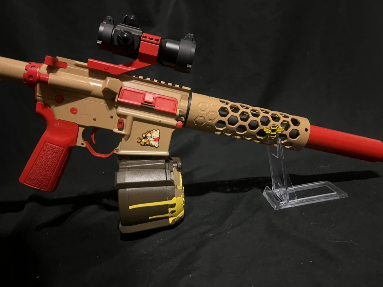 Winnie the Pooh themed custom Cerakote AR-15 with a 7.5-inch barrel in tan and red, honeycomb handguard and honey-drip drum magazine by Tattoo Tactical